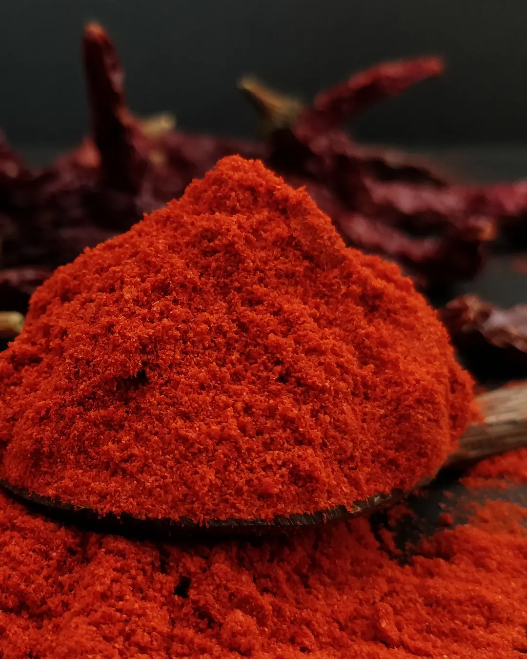 Byadgi chilli powder heaped on a wooden spoon, with whole wrinkled Byadgi chillies behind
